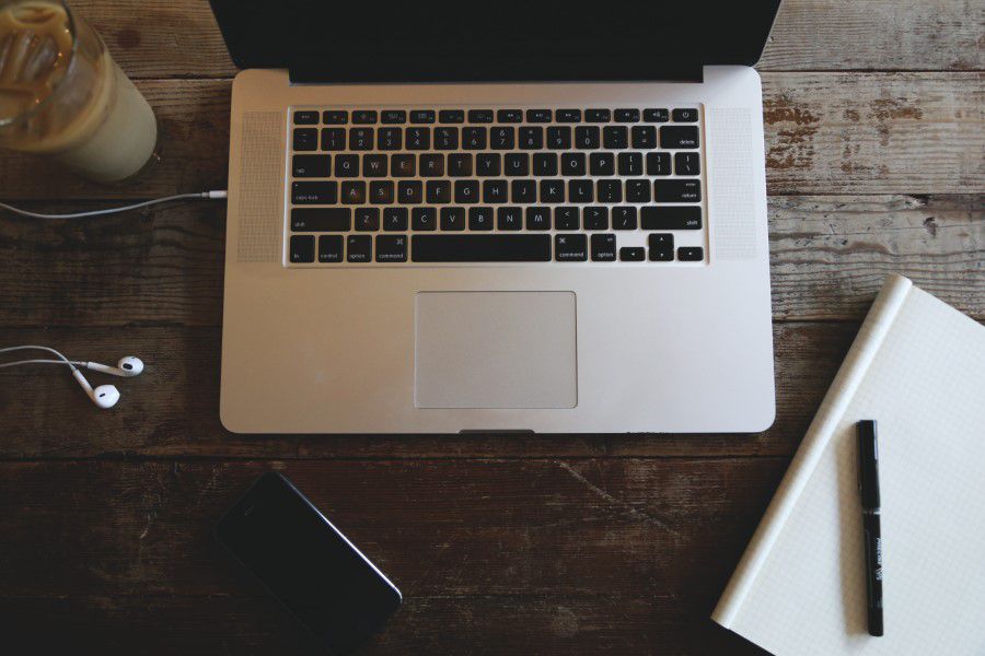 Overhead view of a laptop, notebook, pen and coffee on a wooden desk